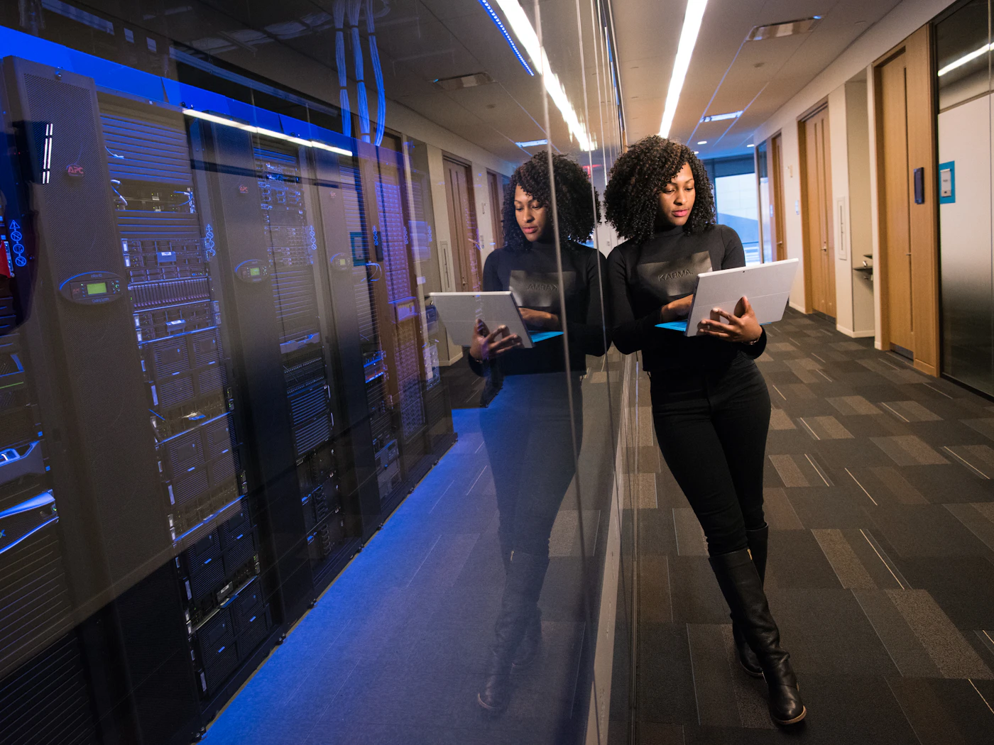 Two people walking a data centre aisle between lit server cabinets, tablets in hand.