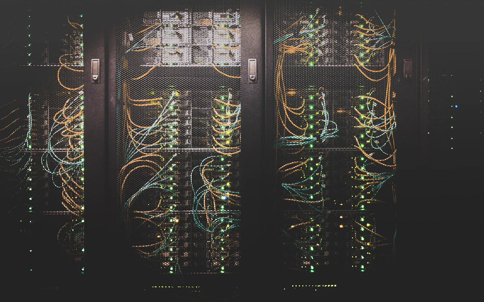 Dark rows of networking equipment in a data centre, patch cables running between racks.