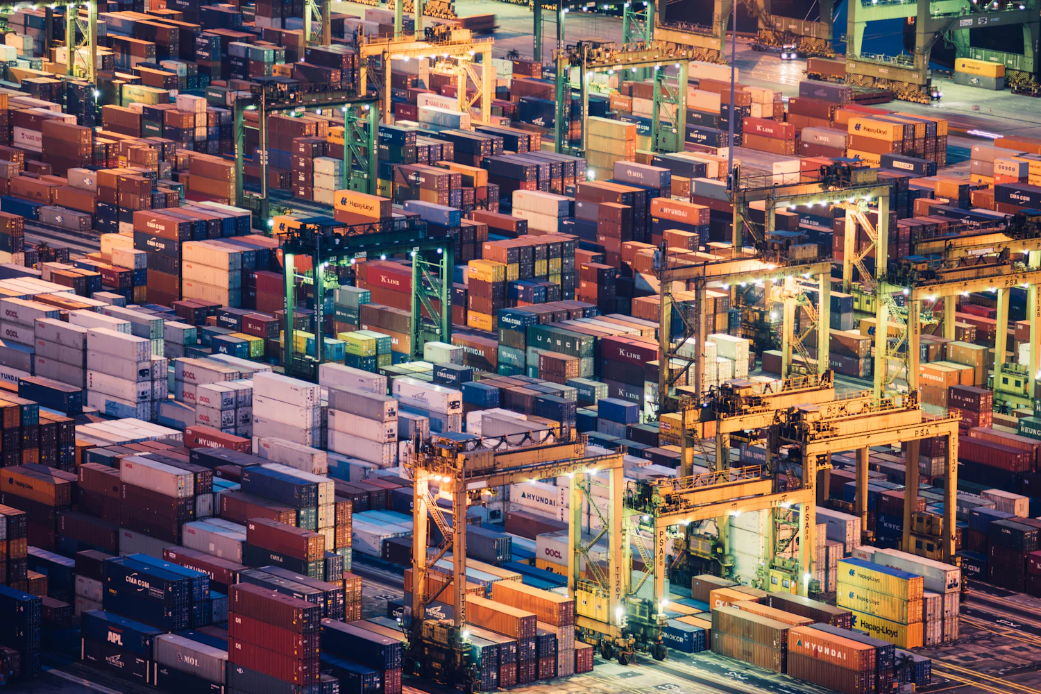 An aerial view of thousands of stacked shipping containers in a port terminal at dusk.